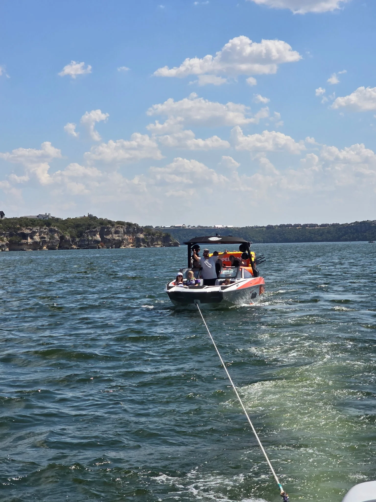 A towed boat and its passengers underway on Possum Kingdom Lake, with the bluffs behind them.